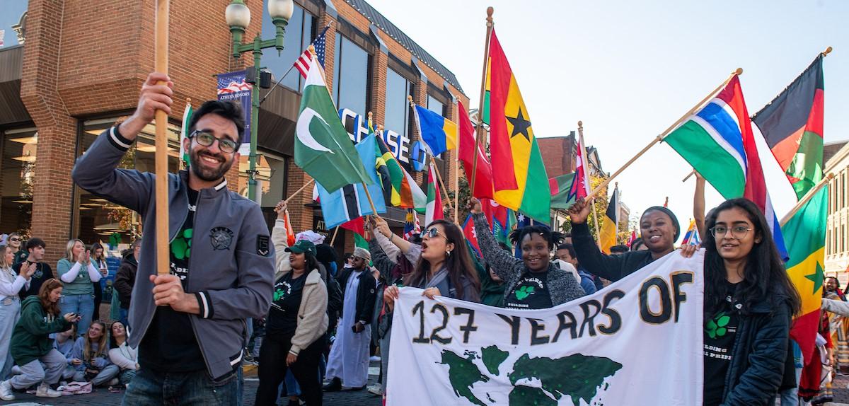 International students walking down the bricks of Court Street with the flags of various countries and a sign that says "127 years of building Bobcat pride."