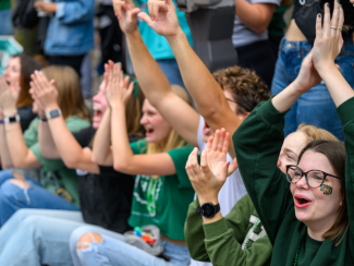 Students cheering in their OHIO gear at the Ohio University Homecoming game. 