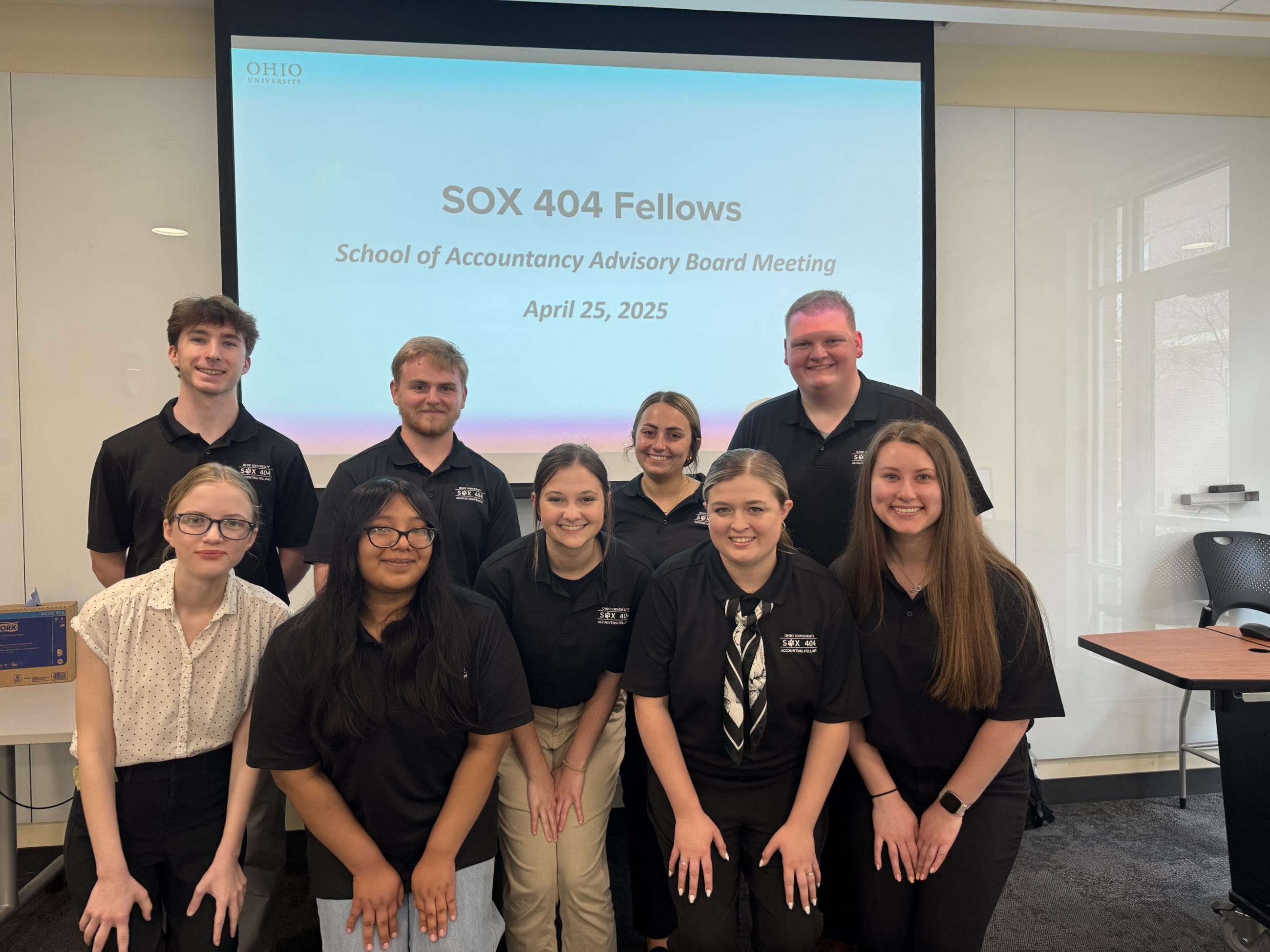Nine members of the SOA board pose in front of a presentation slide