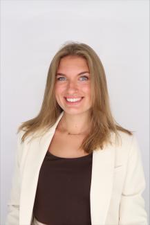 A Headshot of Savannah Dawson wearing an off-white blazer and deep brown scoop blouse, smiling.