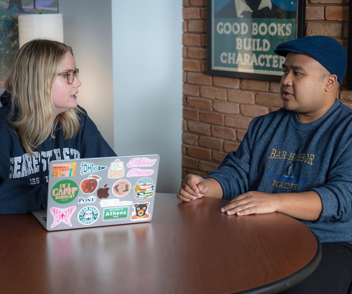 Two students sit together and discuss ideas.