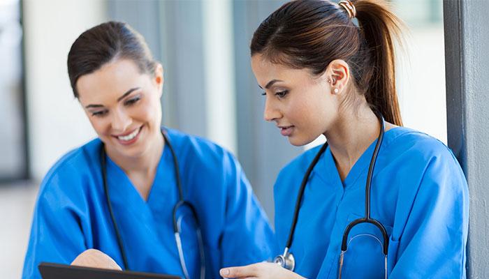 Two DNP students in scrubs reviewing chart on tablet