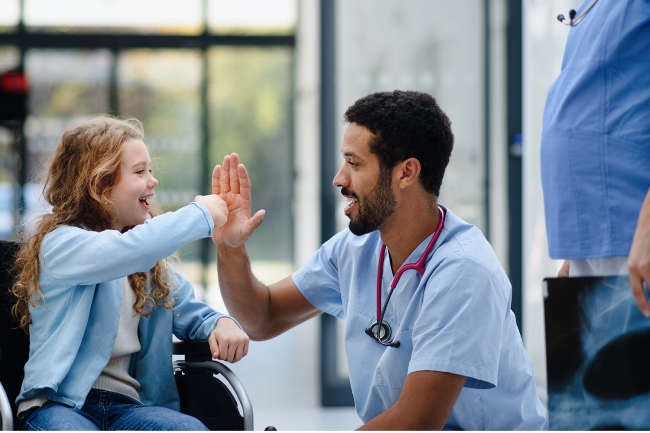 A nurse gives a young patient in a wheelchair a fist bump