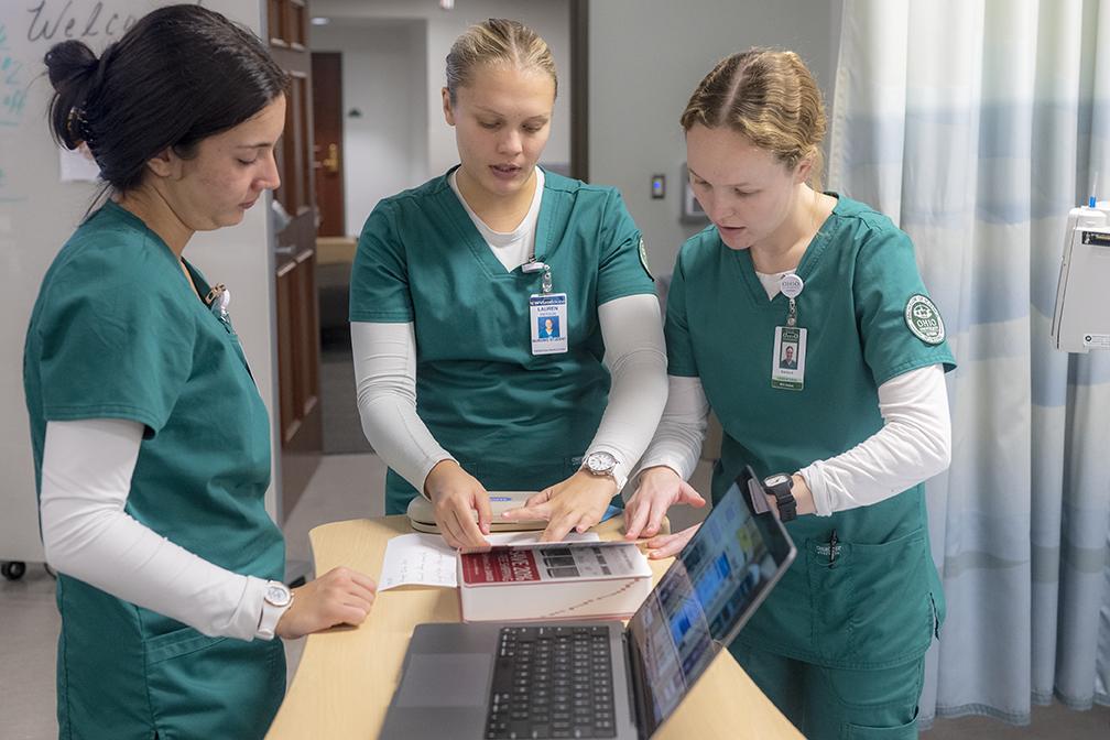 Nurses huddled around desk with laptop and chart