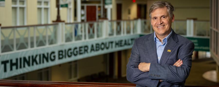 ​ Dr. John McCarthy next to banner that says "Thinking Bigger about Health" 