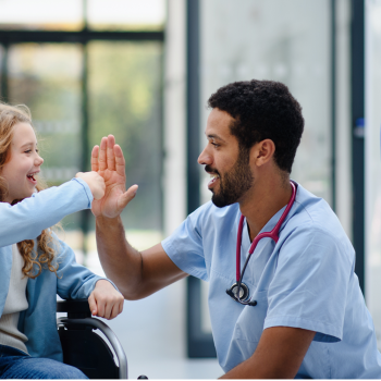 A nurse gives a young patient in a wheelchair a fist bump