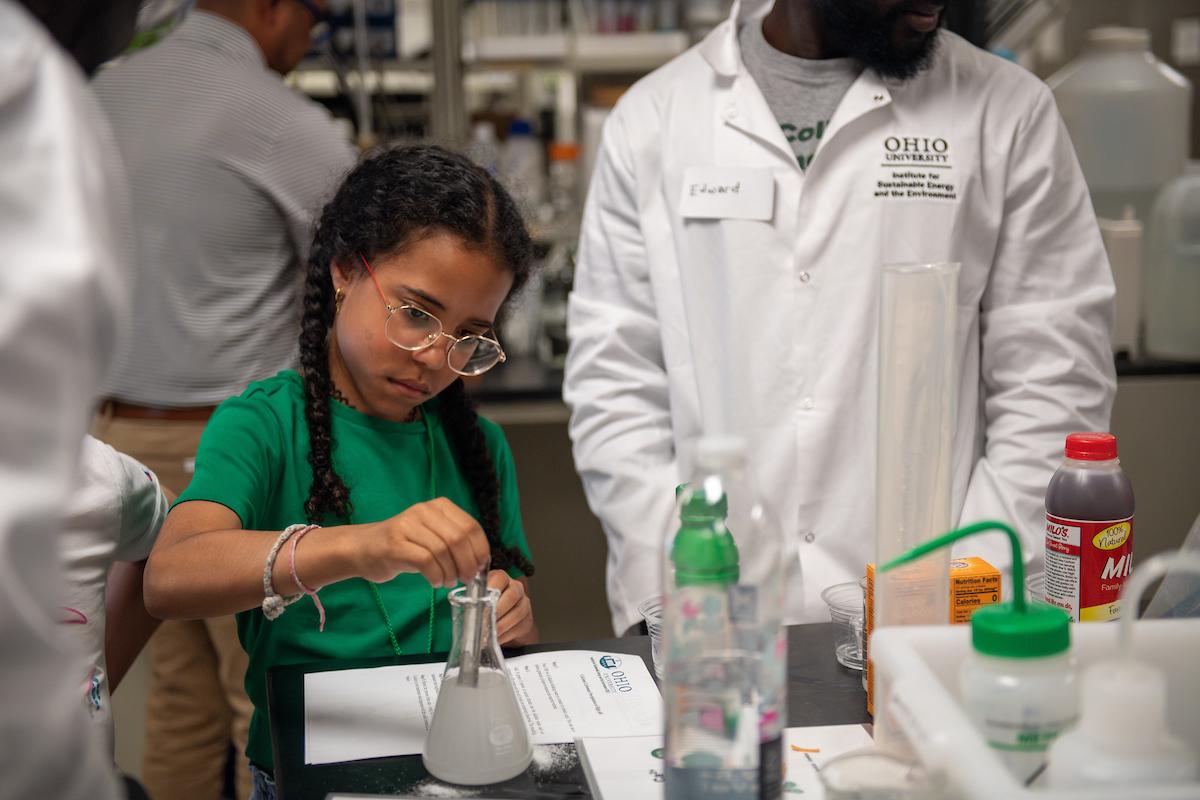 A young girl using a beaker while an adult helps her experiment