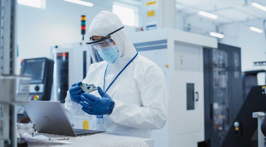 Engineer in protective gear standing at workstation inspecting micro nano device