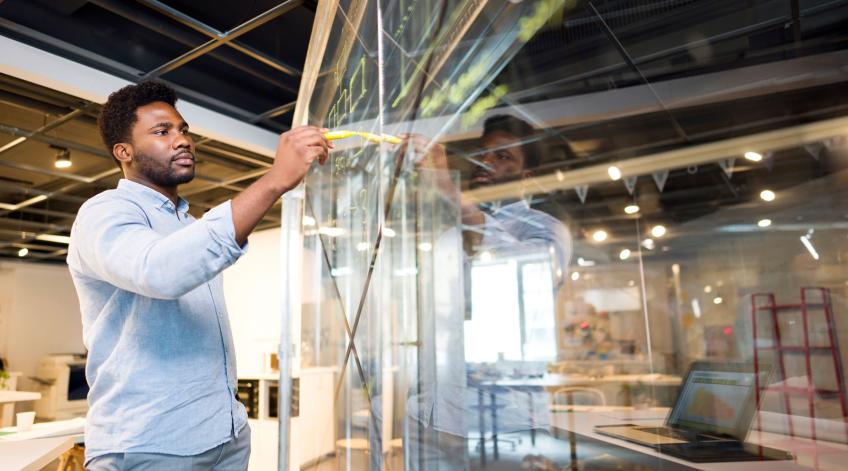 Man at glass board with marker utilizing a lean six sigma certificate to list equations