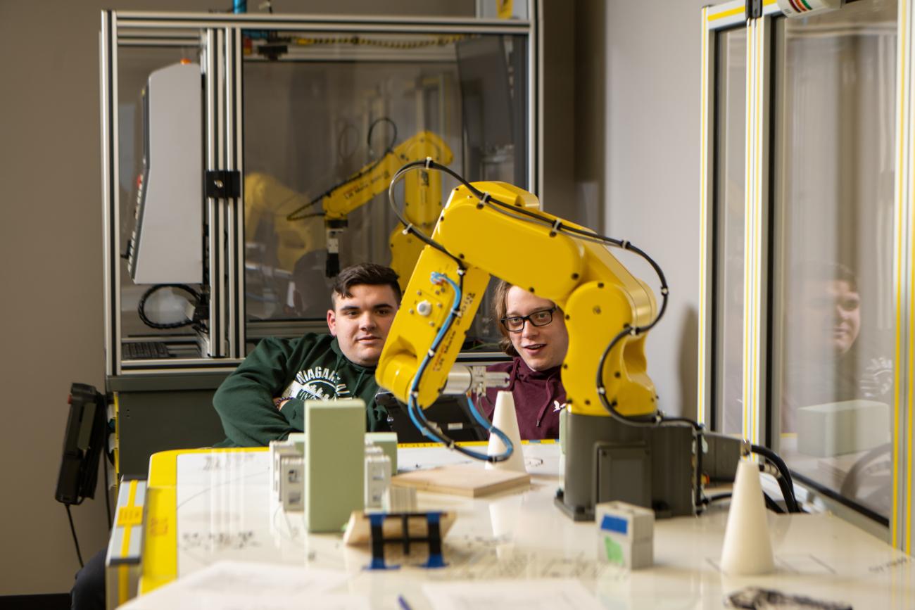 two students watching a robotic arm in a lab