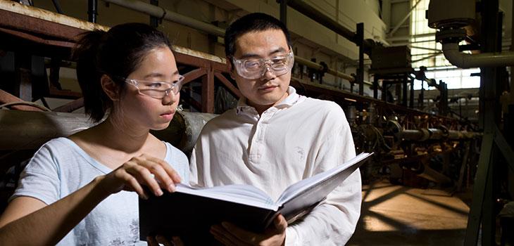 Man and woman reading a book in front of machinery