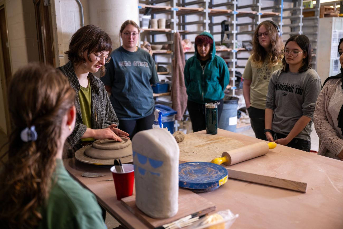 Students listen while a ceramics instructor demonstrates clay techniques in class