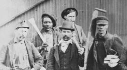 Picture is a black and white image depicting 5 working men posing with the tools of their trade.