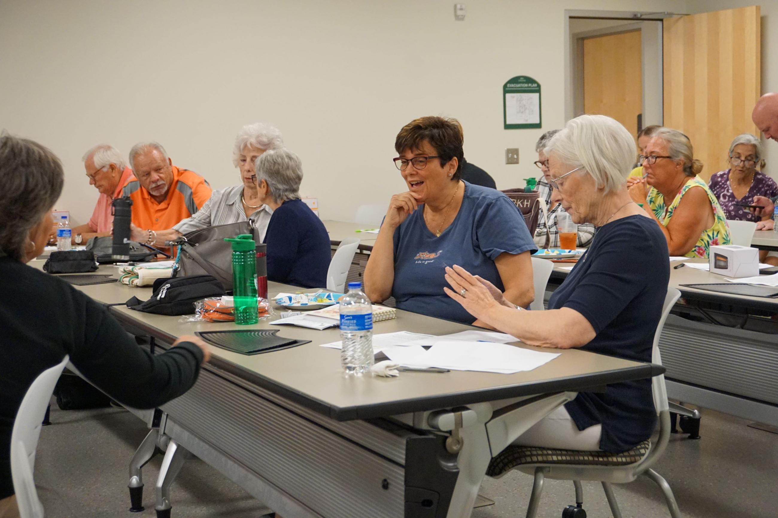 A group of standardized patients sitting at tables talking during a retreat