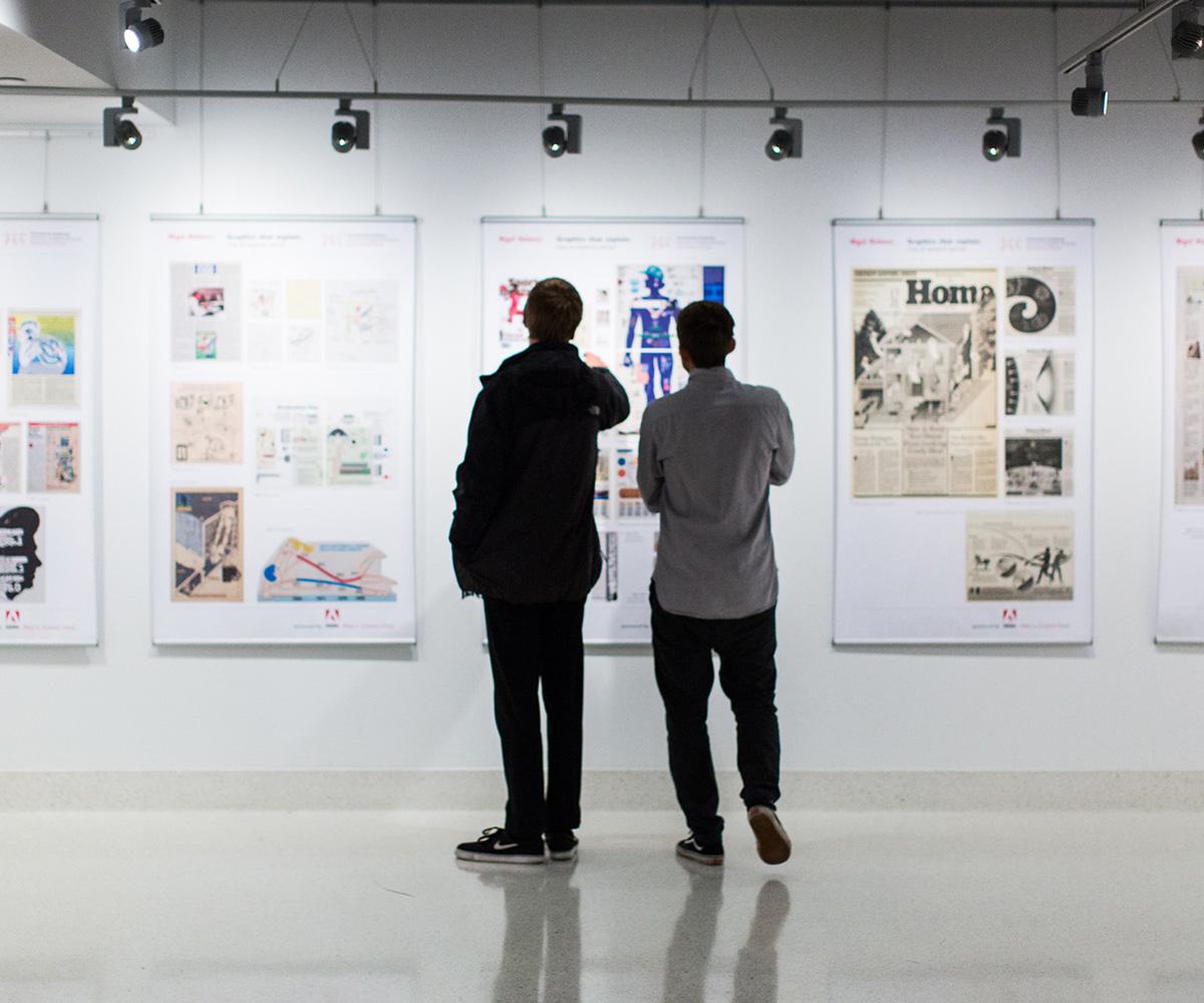 Two people stand in the VisCom Focus Gallery looking at artwork.