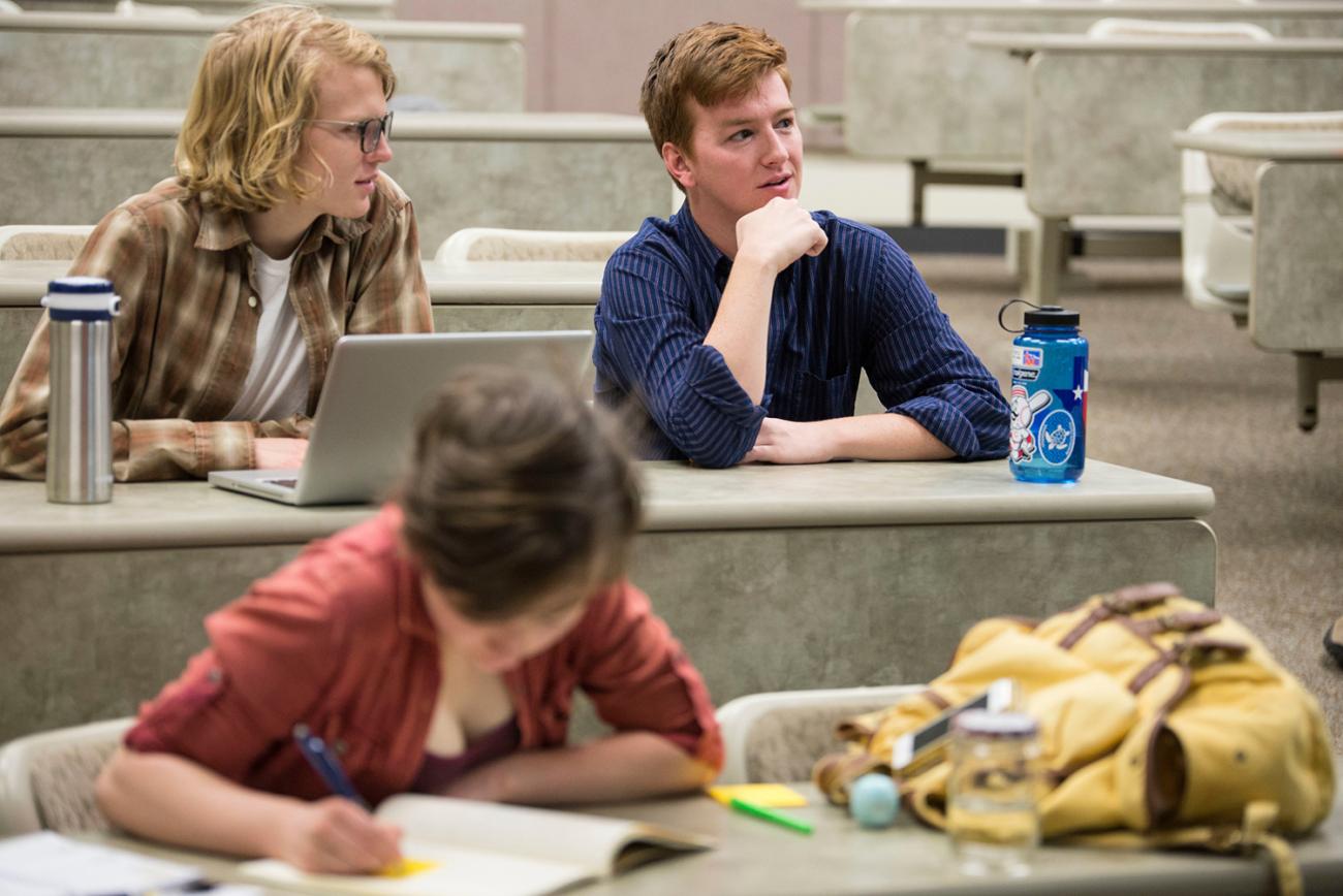 Three students sitting in a lecture hall talking 