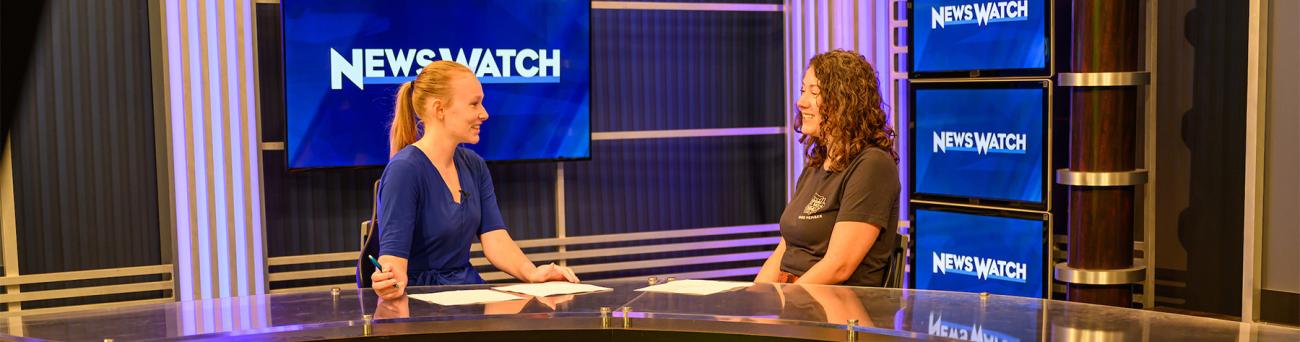 A student news anchor interviews a person during a news segment.
