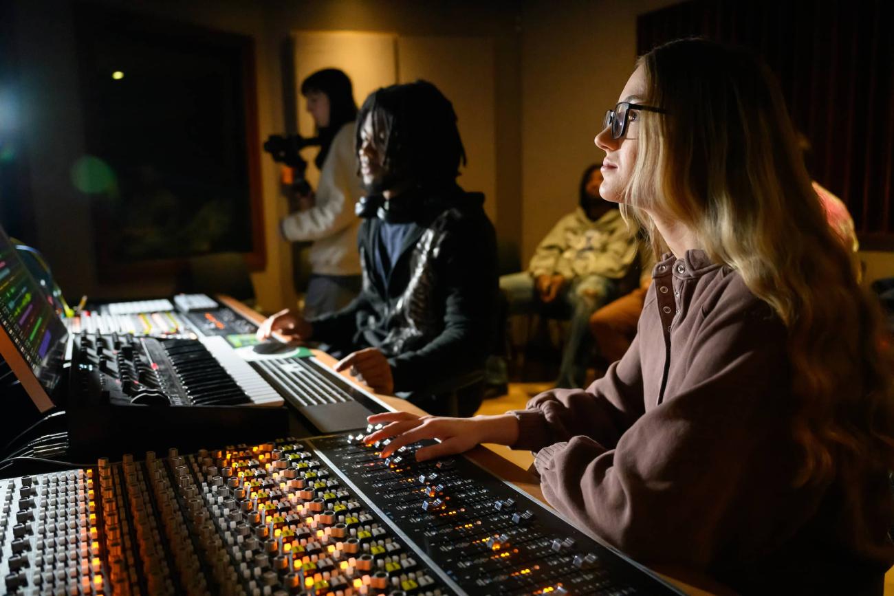Two students work at a sound mixing table in a music recording studio