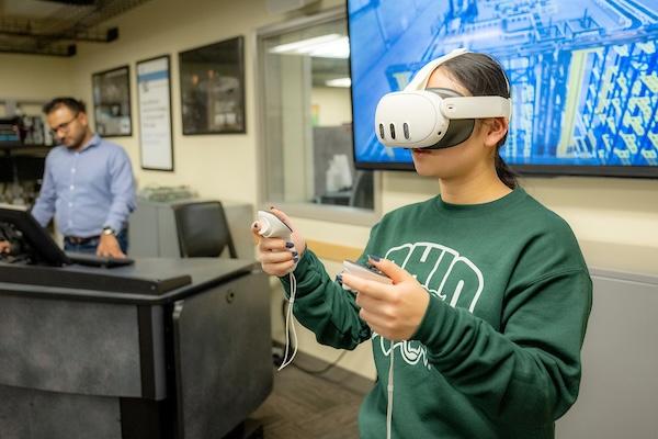 Student working with a VR headset to explore a factory floor where cyberattacks can be simulated.