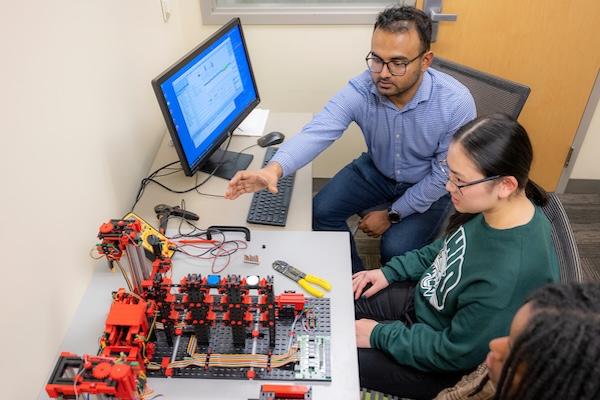 Students and faculty work with an operational technology factory simulation setup.