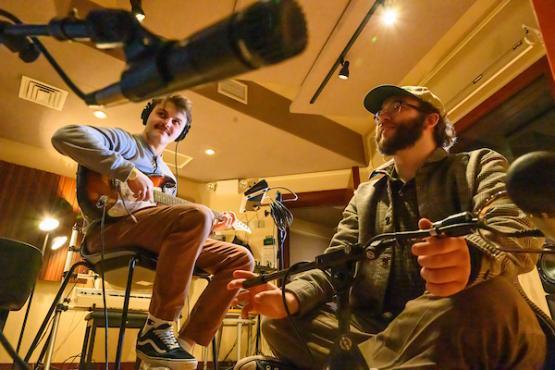 Man playing the guitar while another man is recording his sound