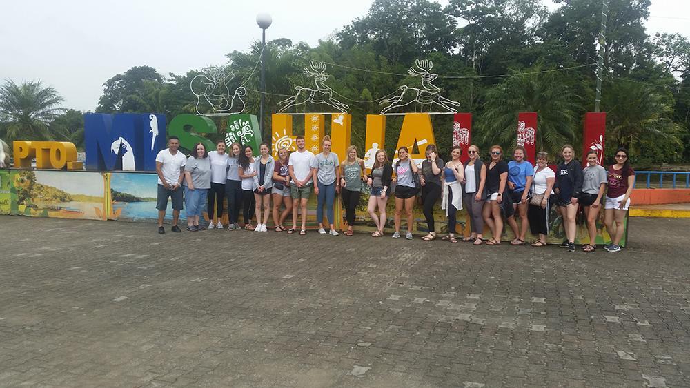group of students standing in front of a large sign