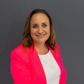 a woman smiling facing the camera wearing a hot pink blazer and white shirt with brown and blond shoulder length hair
