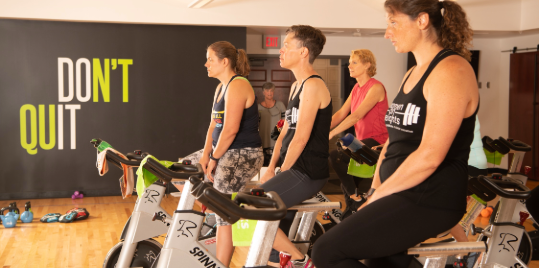 WellWorks members in a Spin Class with the words Don't Quit on the wall.