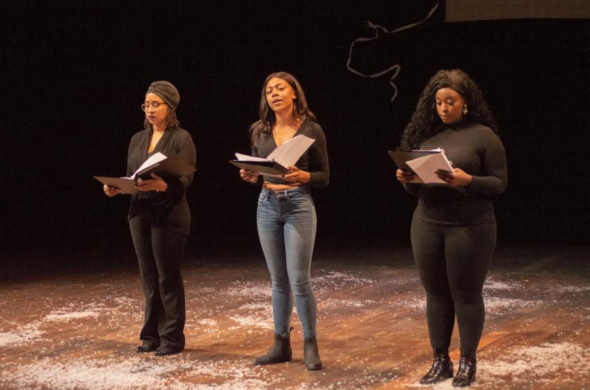 Three women read scripts on stage