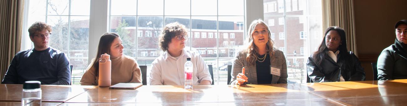 Six students sitting at a table with the sun shining through the windo behind them