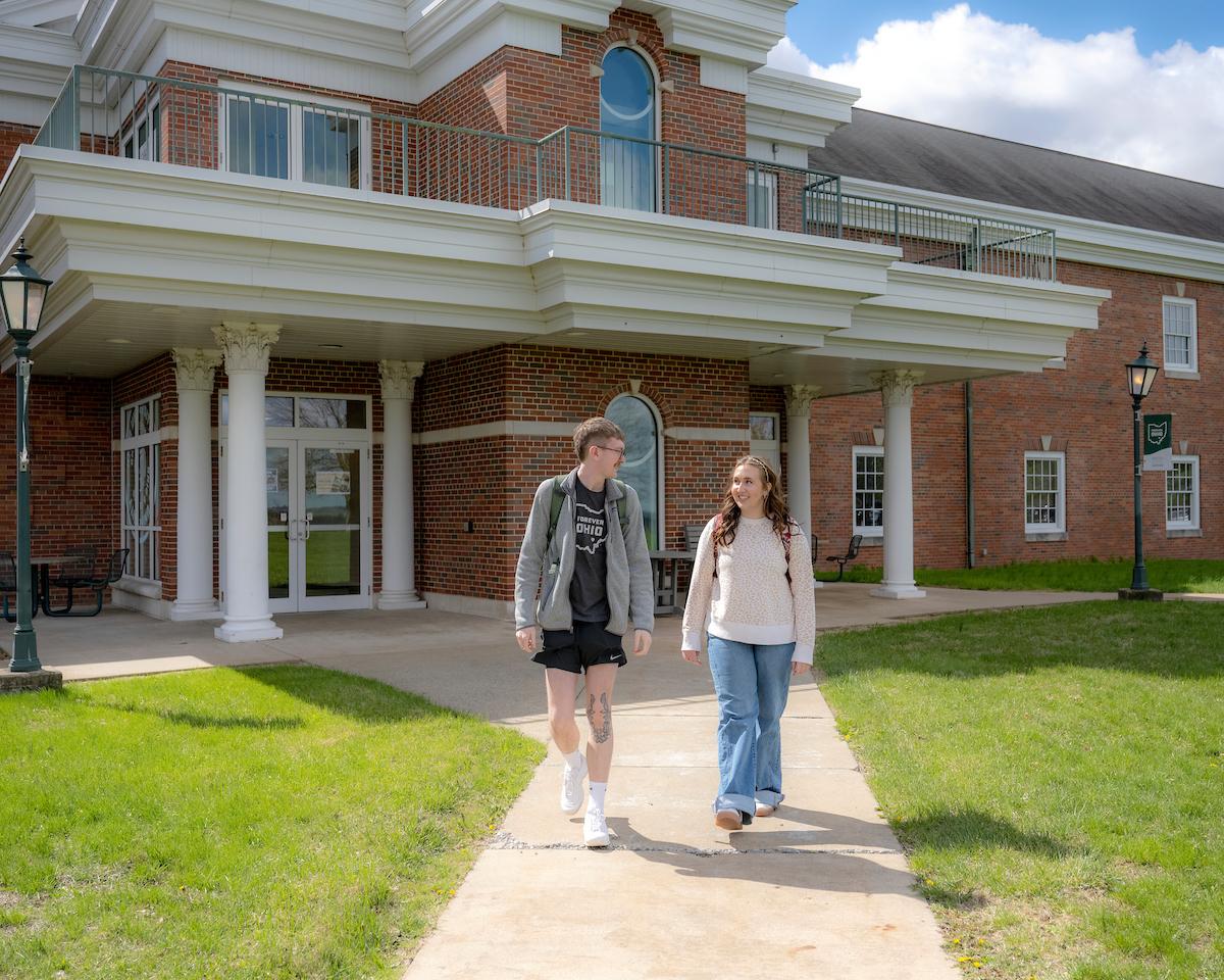 OHIO Eastern Current Students, One tall male, one female walking on a sidewalk in front of the building
