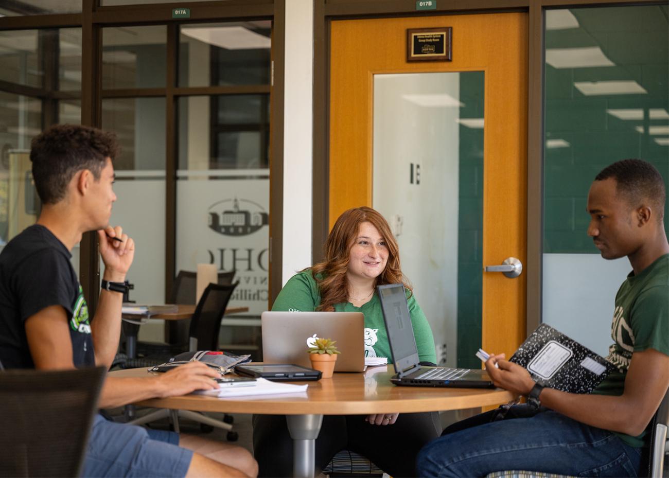 Three students work on school work at a table together.