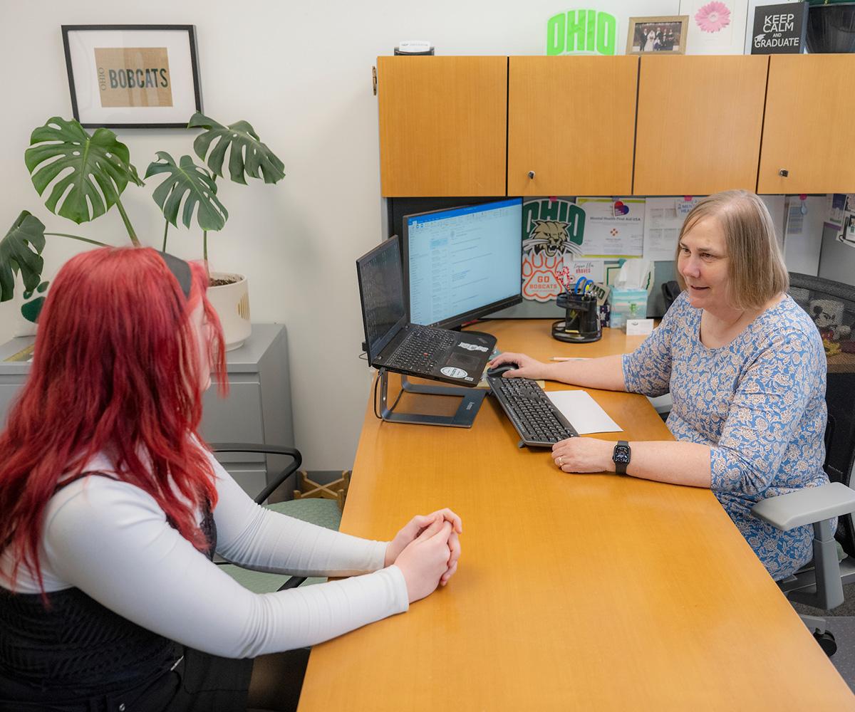 An advisor and student have a conversation while sitting at a desk.