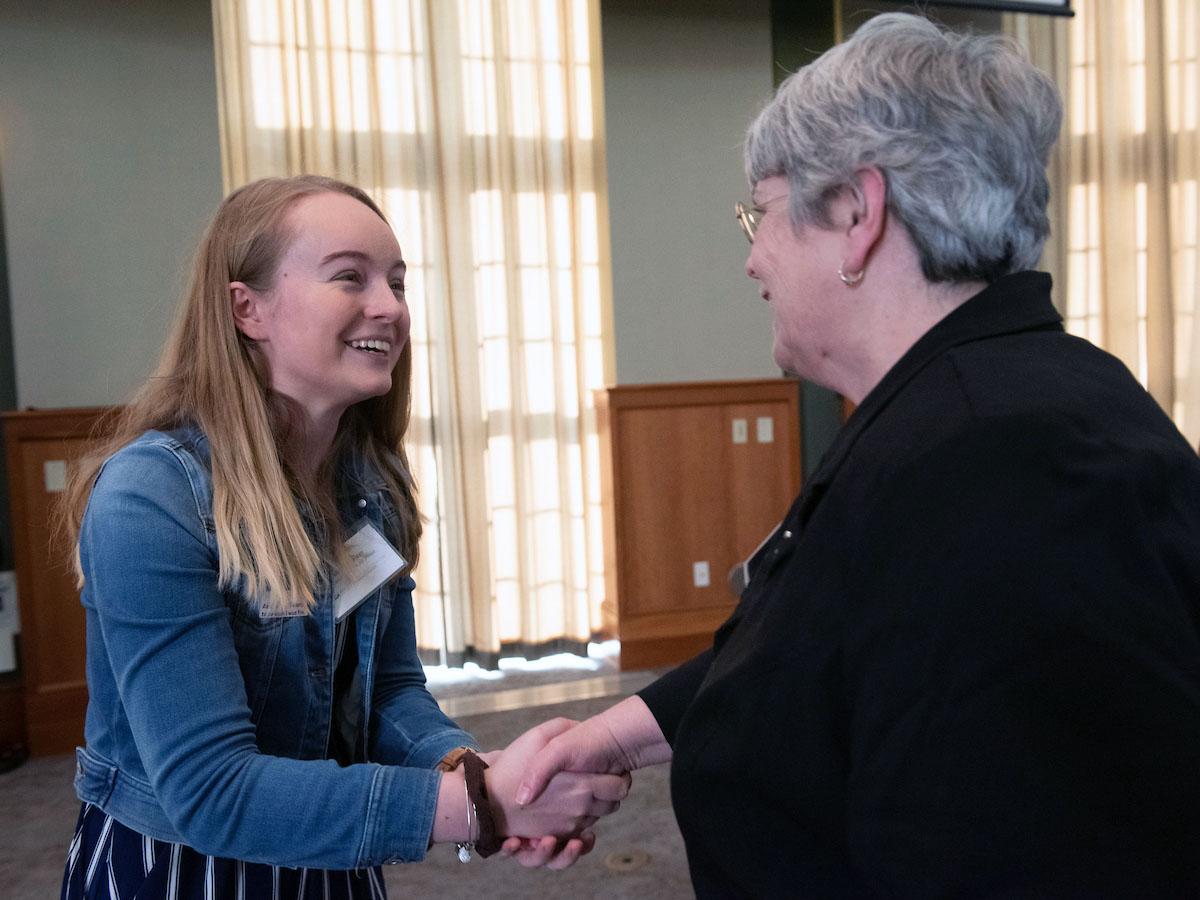 A young woman shakes hands with an older woman.