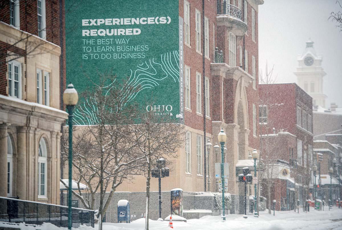 Snow falls on a street view looking at an academic building on Ohio University's Athens campus.