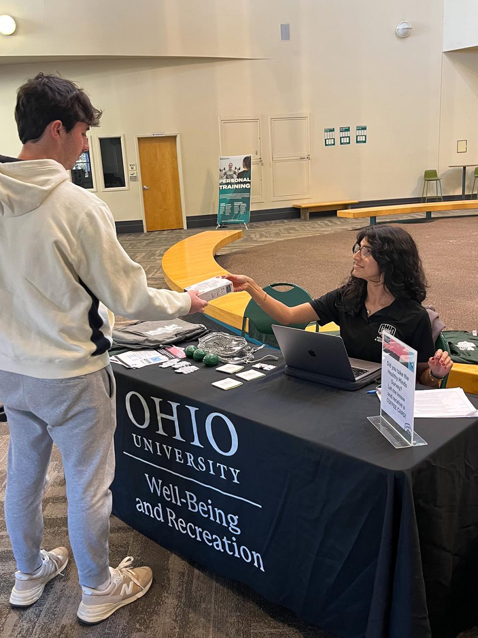 Woman sitting at a table handing out items to students who complete survey