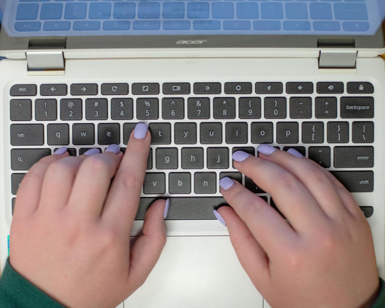 Two female hands with lilac purple fingernail polish typing on a keyboard
