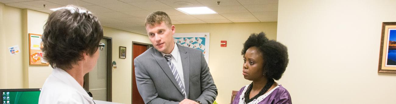 Two hosptial employees talk to a doctor at a desk.