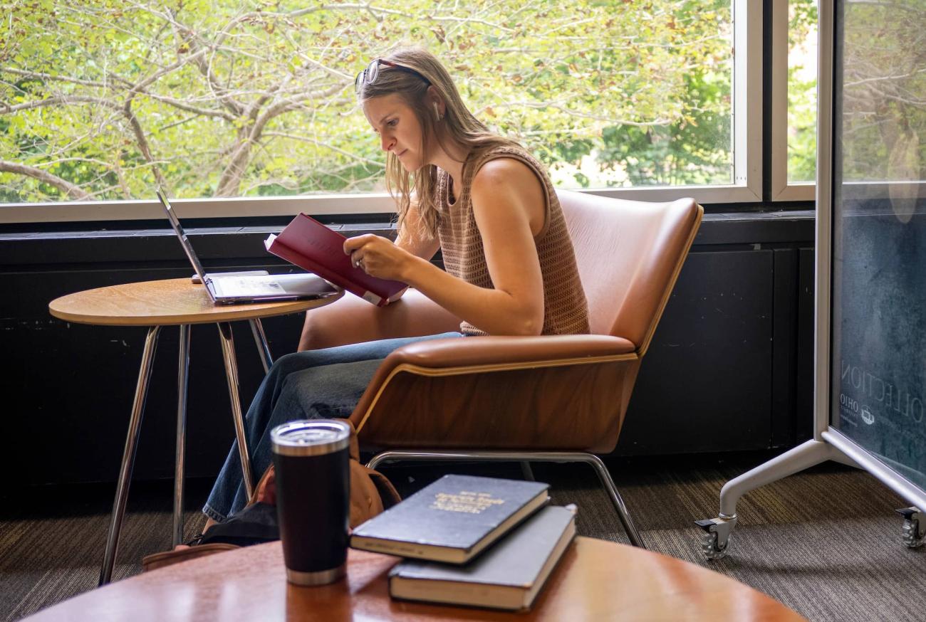 A student studies at the library surrounded by books and their computer
