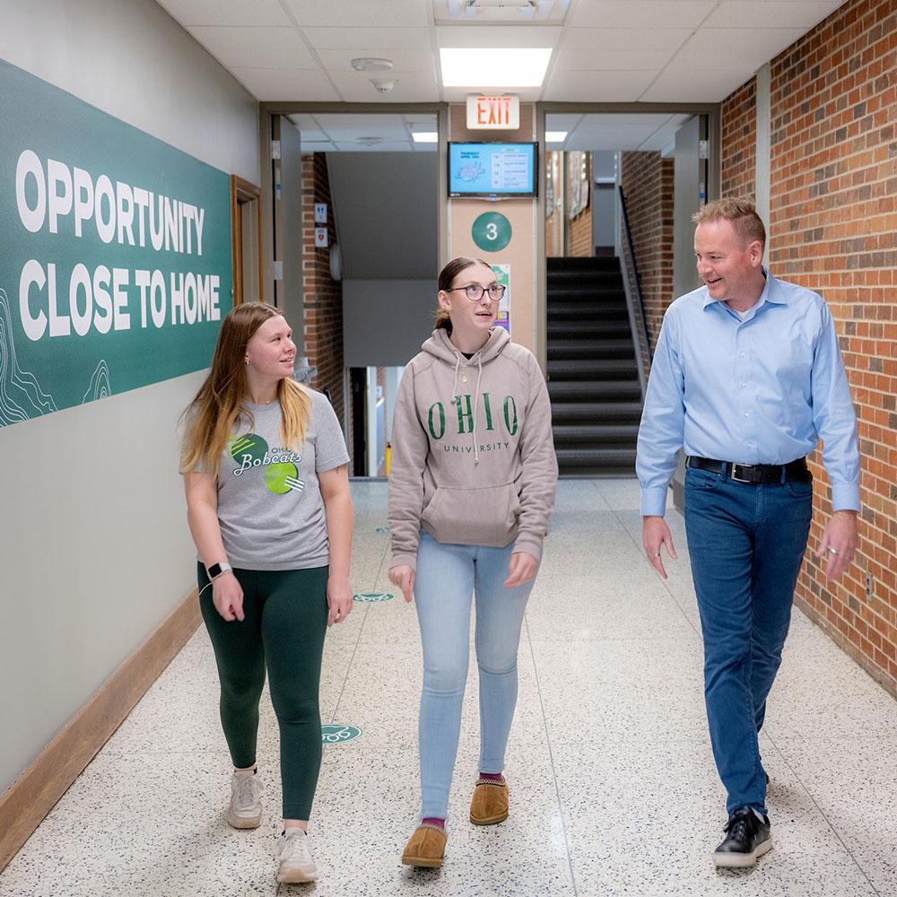 Two students walk with a campus staff member while talking.