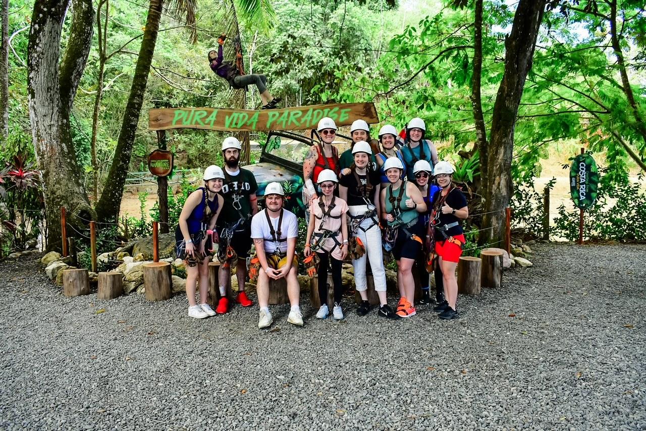 A group of students wearing helmets stand together in front of a lush green forest