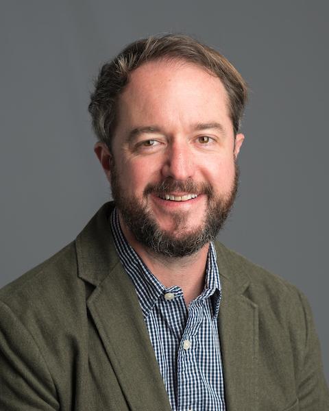 Person wearing green sport coat and blue shirt.
