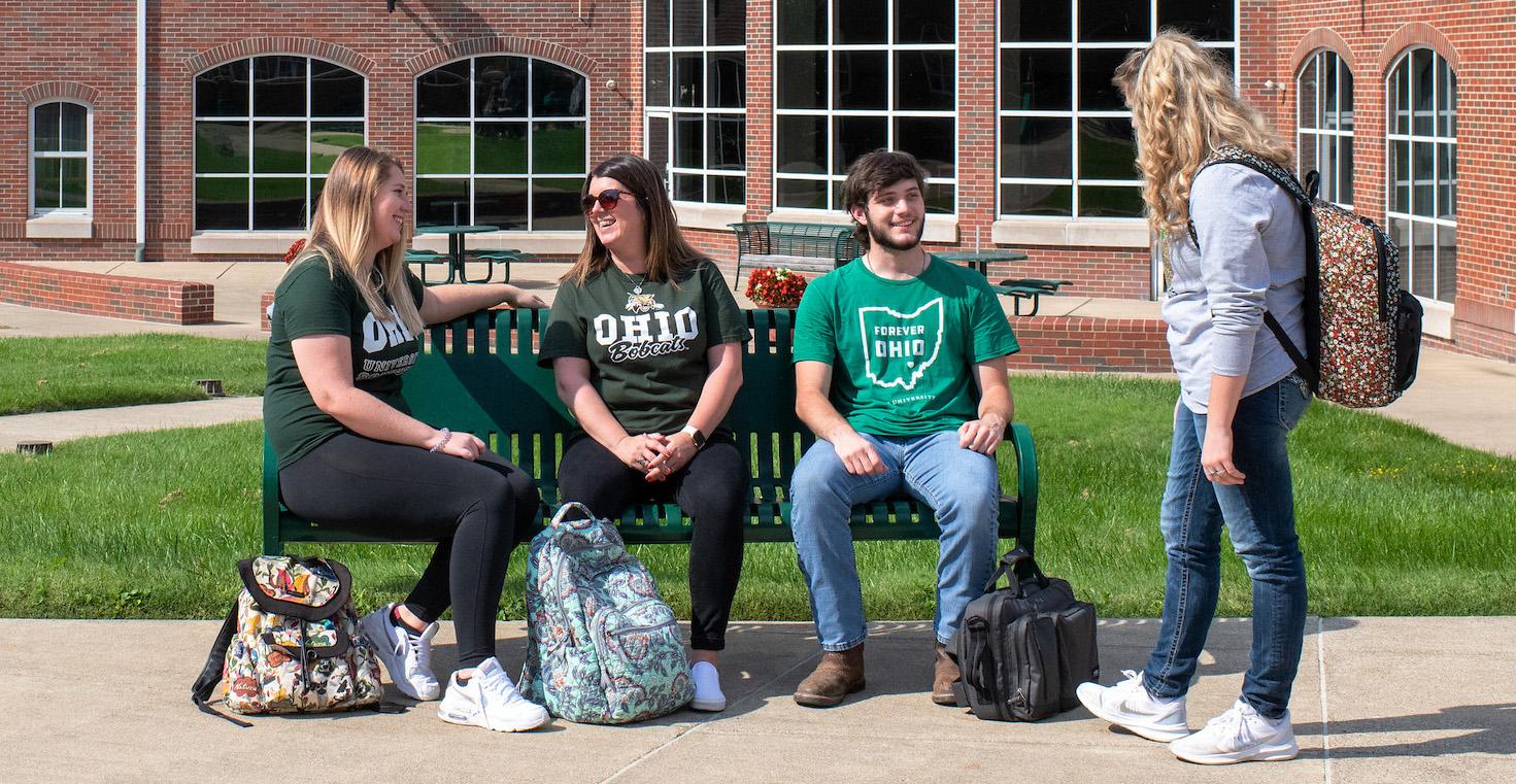 students talking while sitting on a bench outside