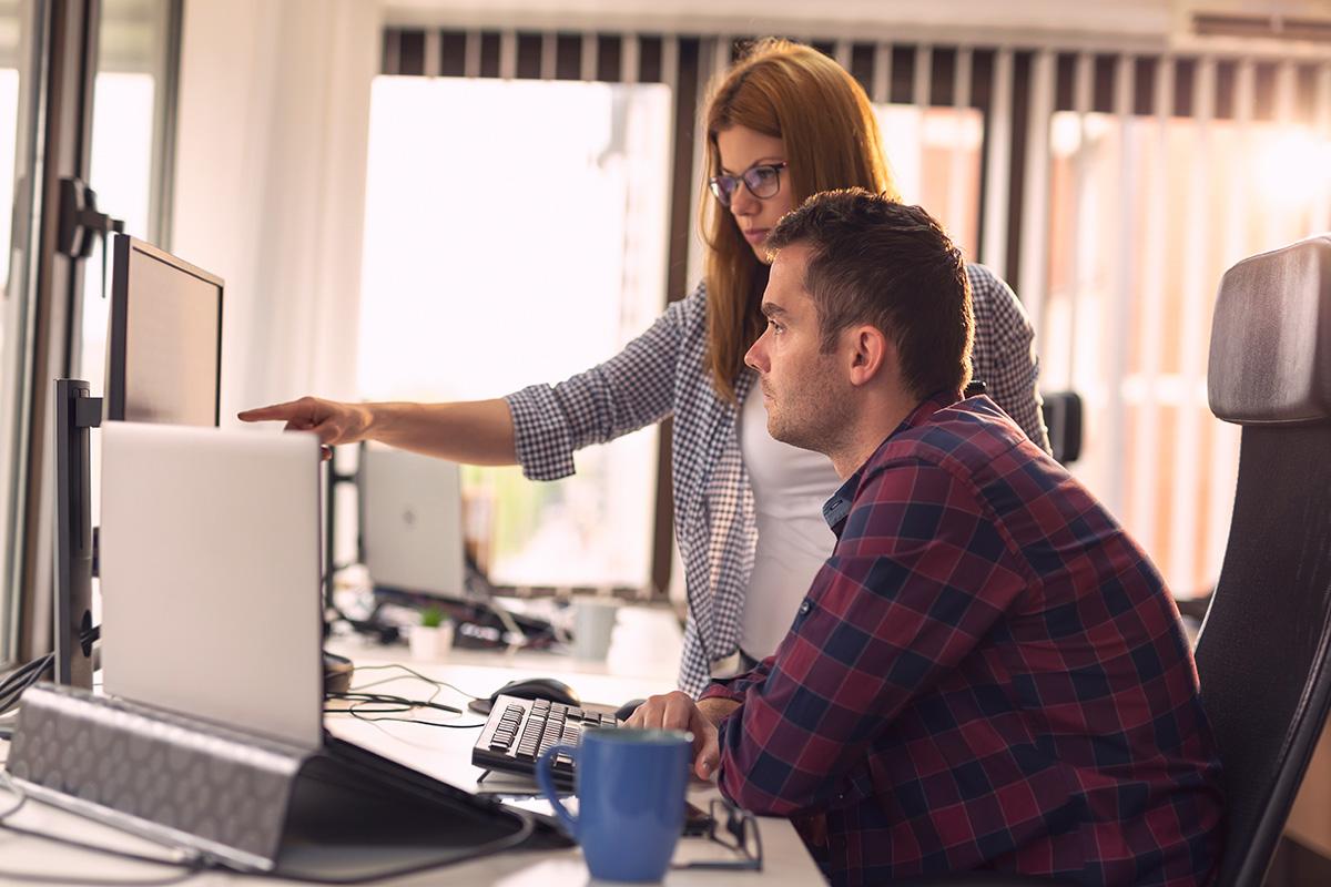 One person helps another person who is working on a computer.