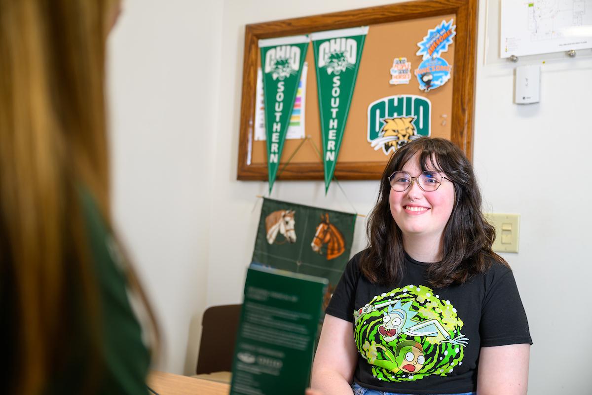 student smiling while sitting in front of university staff member's desk