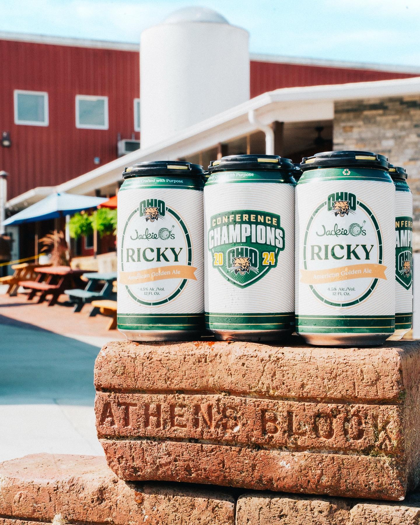 Three cans of Jackie O's Ricky beer with MAC Champions commemorative designs, sitting on an Athens Block brick