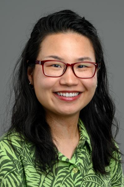 A headshot of a woman with a green shirt, dark hair and red glasses