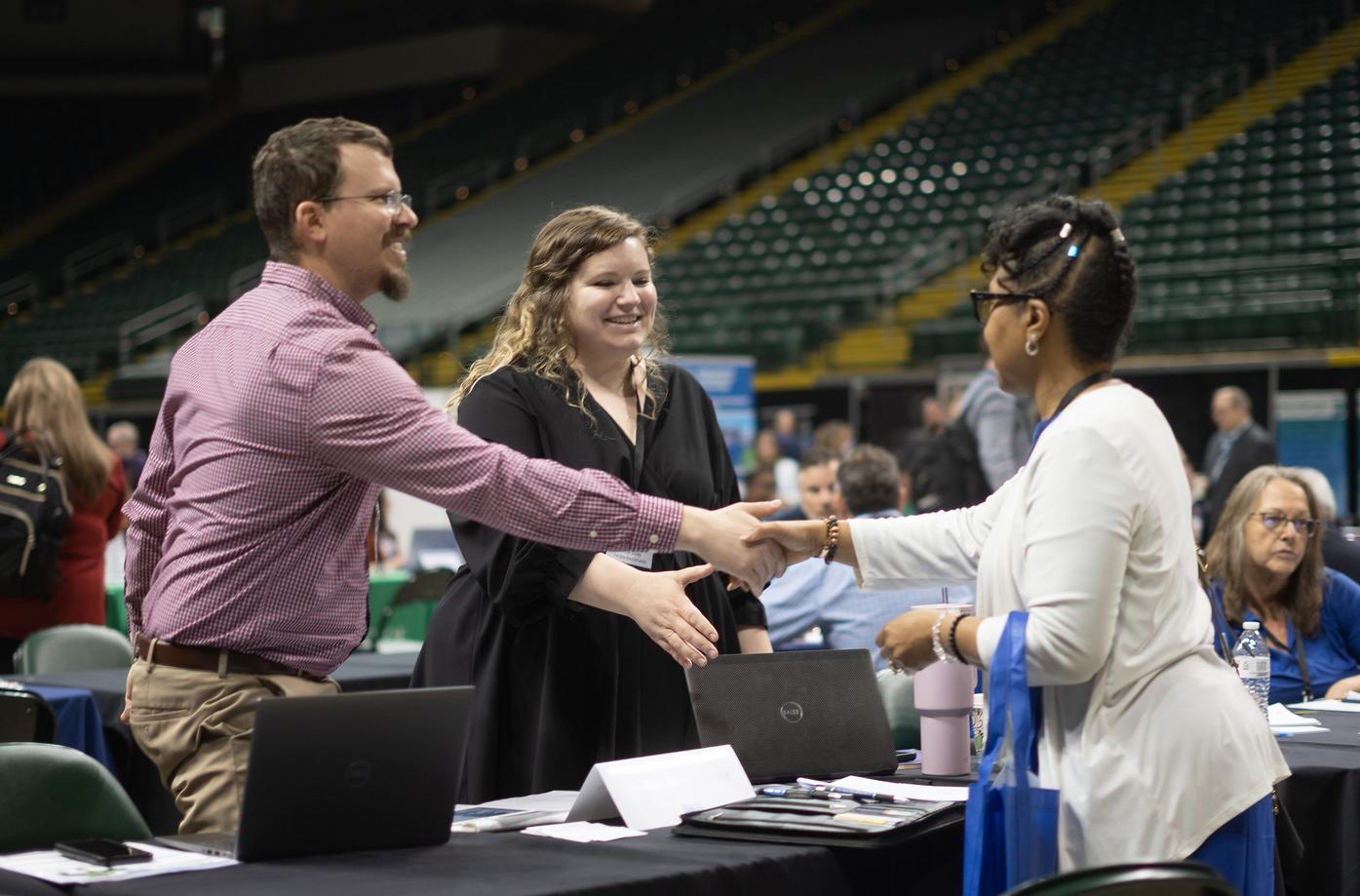 Three individuals are greeting one another by shaking hands. 