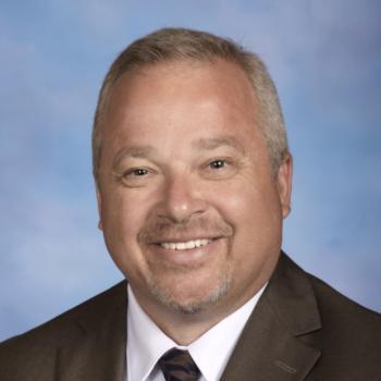 Smiling man with short hair gray suit jacket, tie and white shirt with a blue background